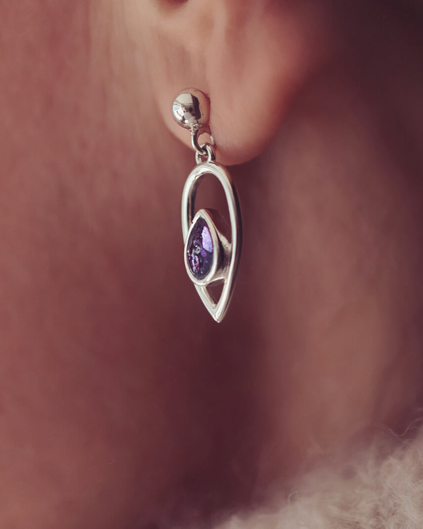 Cremation Ashes Peardrop Dangle Earrings filled with purple crystal and ashes, worn in a ladies ear