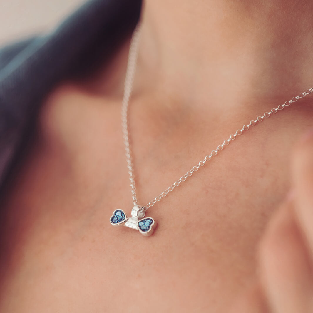 sterling silver bone shaped necklace, filled with cremation ashes, blue crystal and resin on a silver chain around a ladies neck