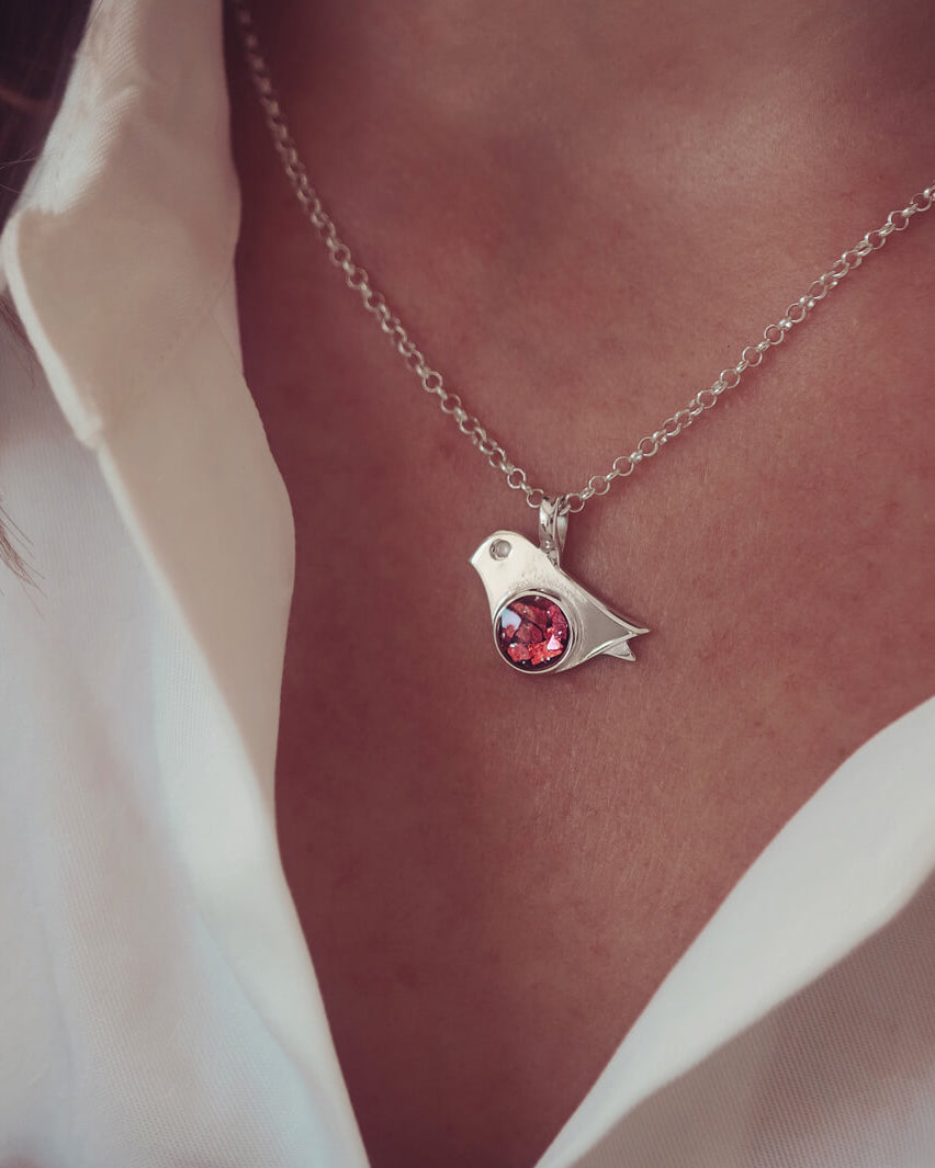 sterling silver robin necklace holding cremation ashes and red crystal, on a ladies neck