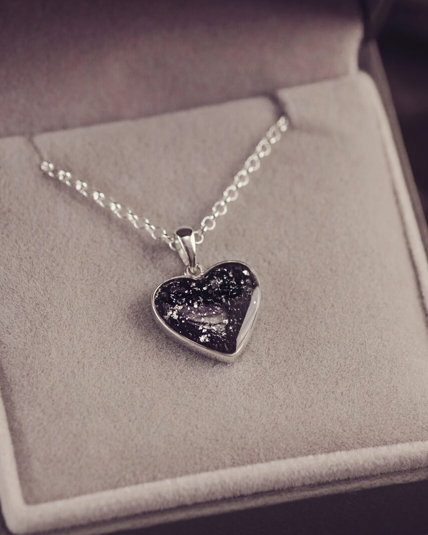 Sterling silver heart necklace with a central section filled with memorial ashes and black crushed crystals, displayed in a grey jewellery box
