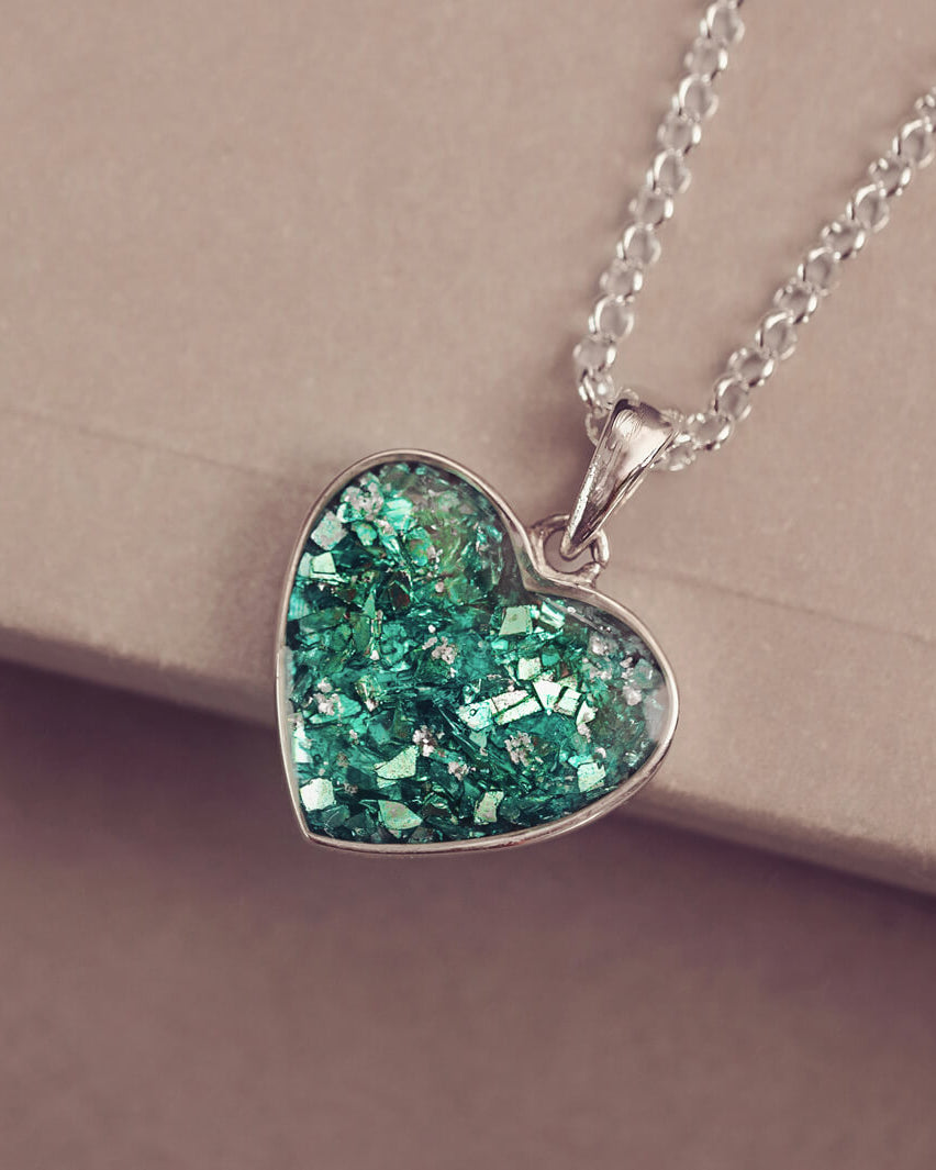 A small heart pendant, in sterling silver, filled with green crystals and cremation ashes, covered with resin
