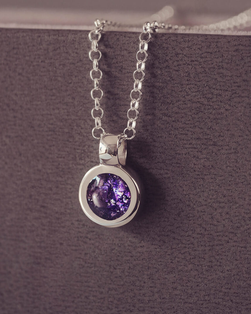 Sterling silver round necklace with a central section filled with memorial ashes and purple crushed crystals, displayed on a grey background