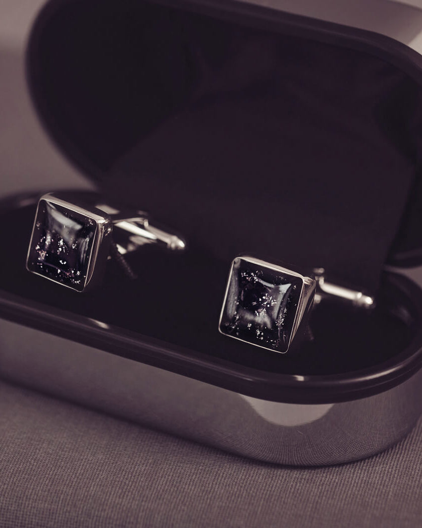 Square silver cufflinks containing cremation ashes, black crystal and resin sat in a black and silver cufflinks case