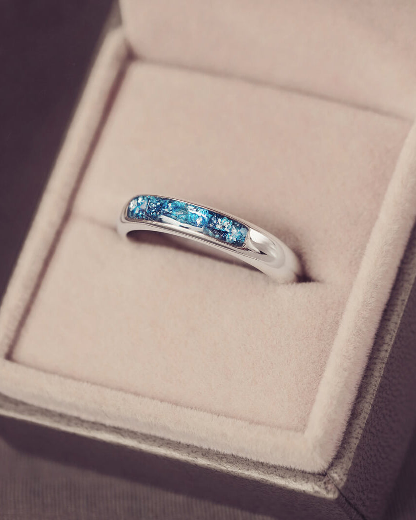 Sterling silver womens ring band with a central section filled with  memorial ashes and blue crushed crystals, displayed in a grey jewellery box