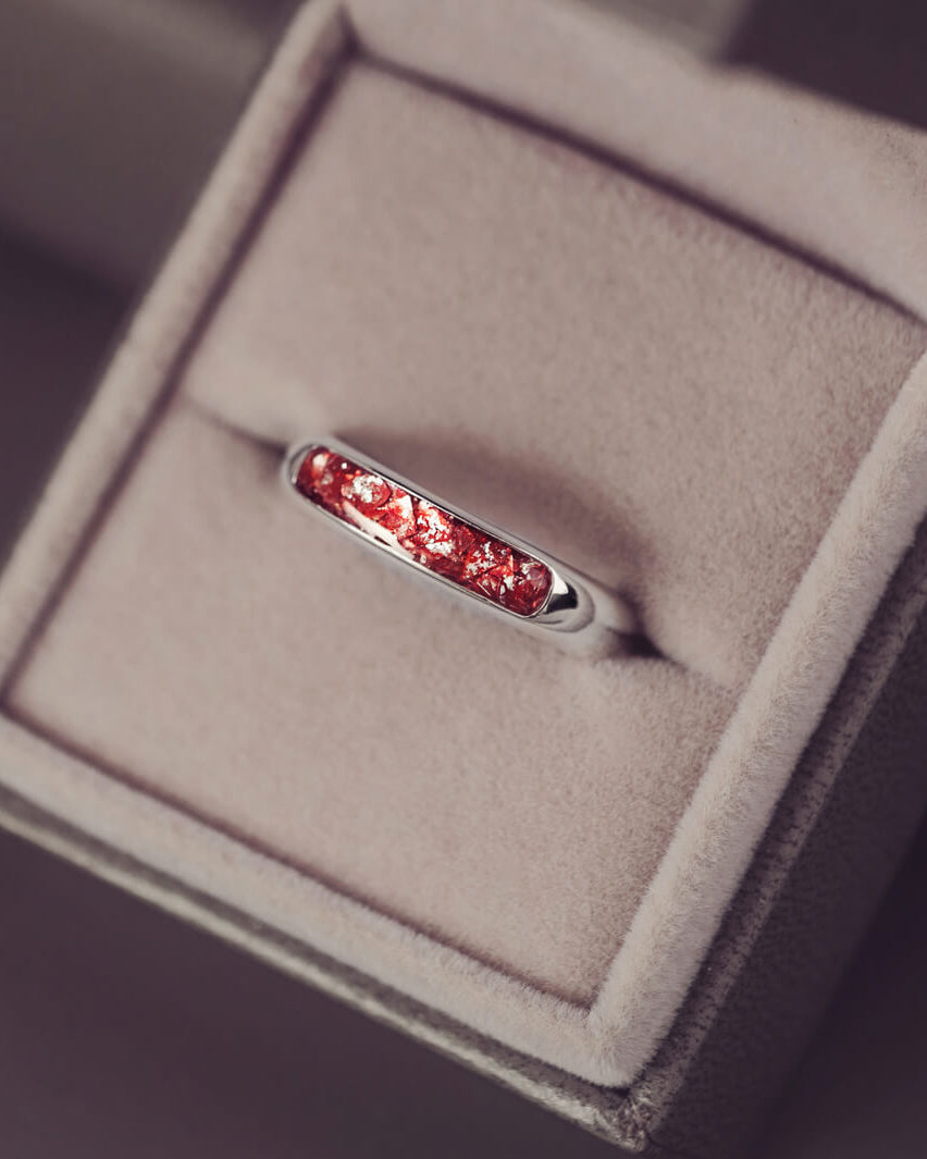 Sterling silver womens ring band with a central section filled with  memorial ashes and red crushed crystals, displayed in a grey jewellery box