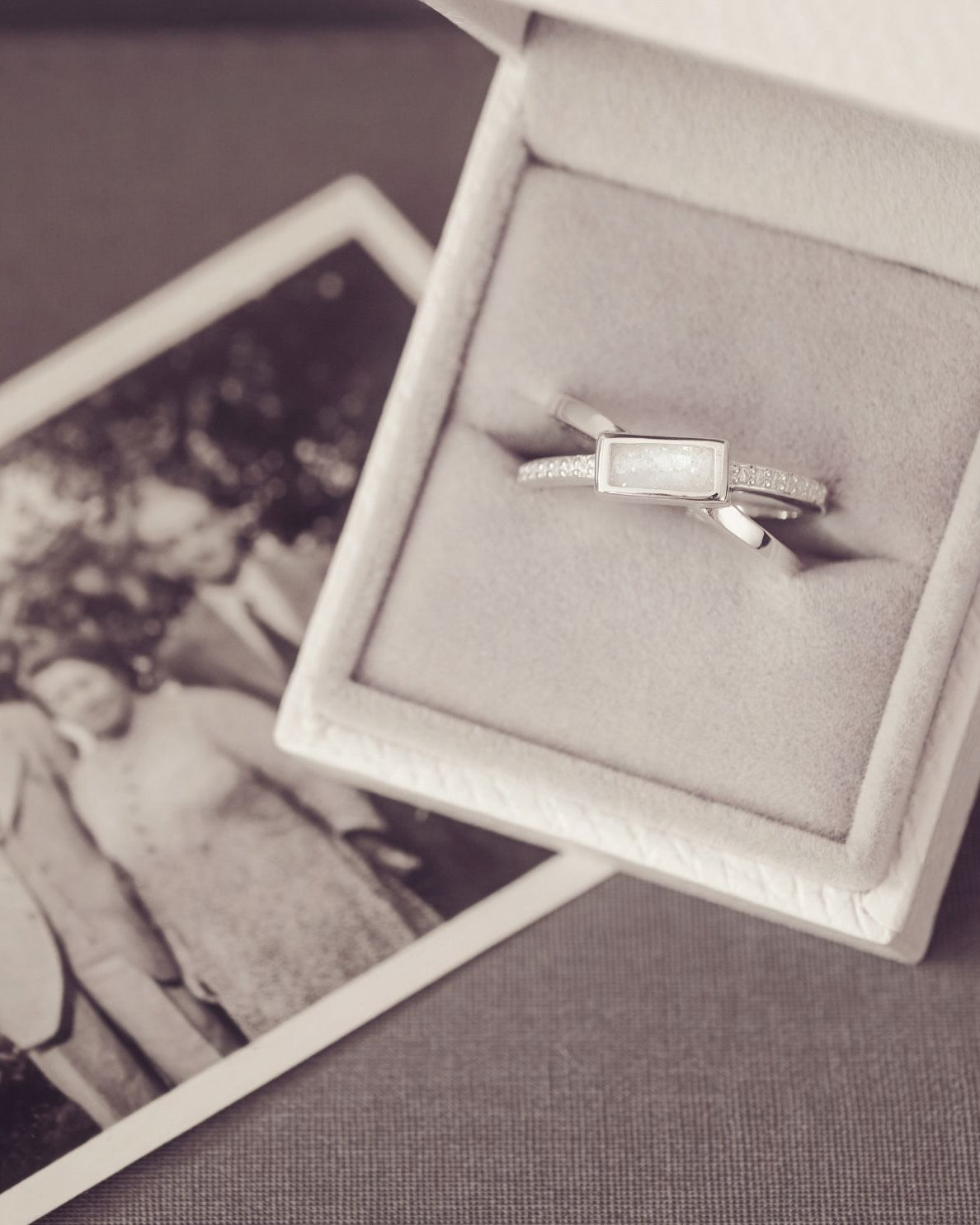 Silver ring in a box with an old photograph of two people in the background