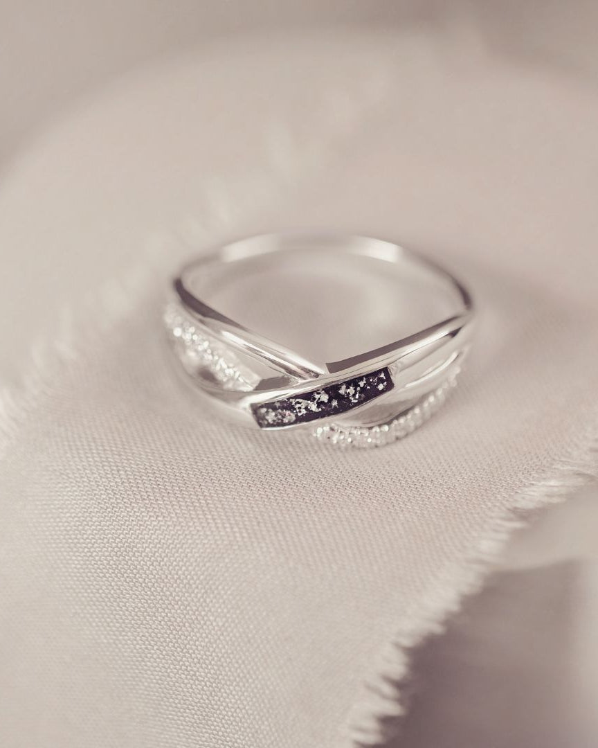 Silver ring with a small black inlay on a soft fabric background