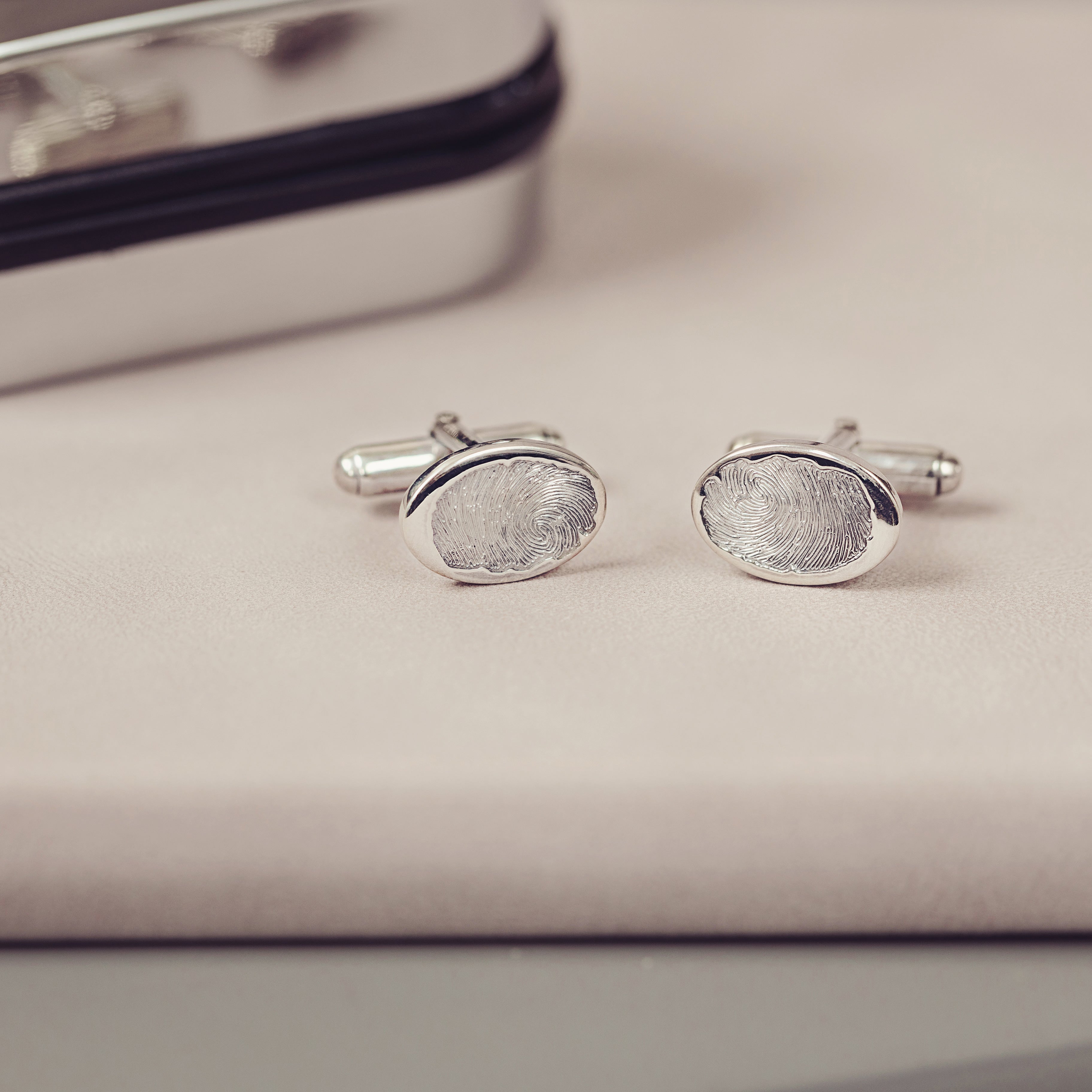 A pair of silver fingerprint cufflinks with a silver cufflink case displayed next to them