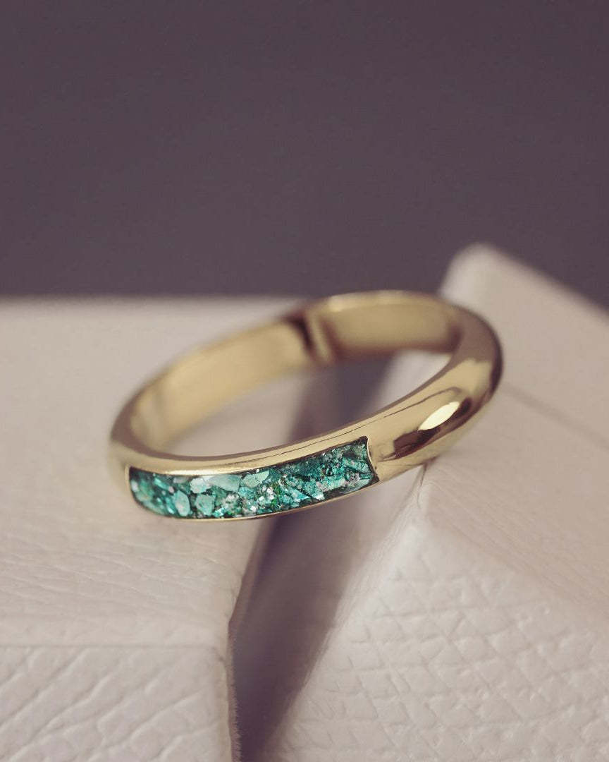 Gold ring with green gemstones on a textured surface
