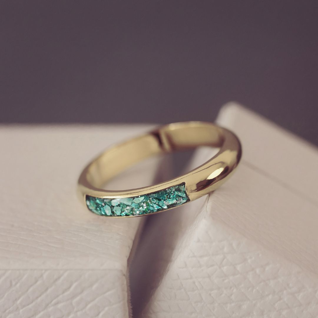 Gold ring with green gemstones on a textured surface