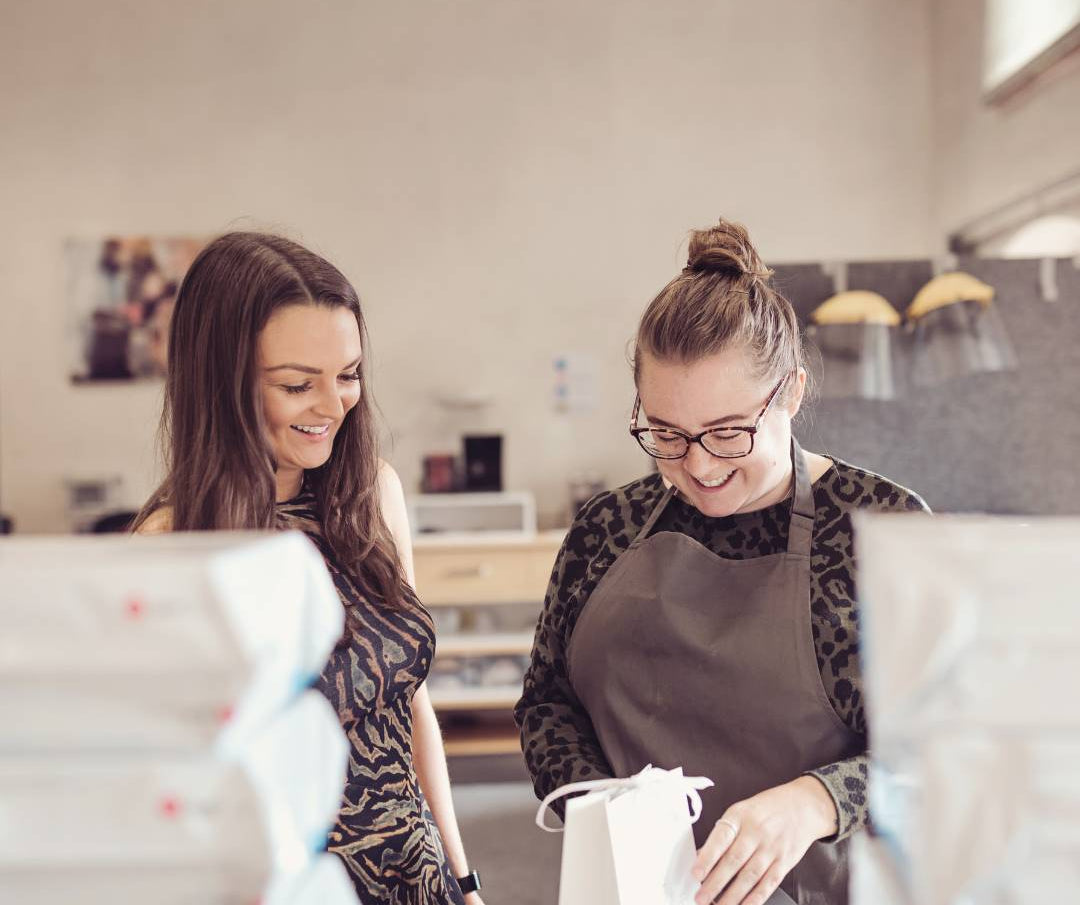 Two ladies standing in a workshop packing jewellery boxes