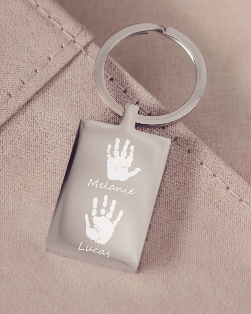 A stainless steel keyring, engraved with two handprints and names, on a pink fabric background