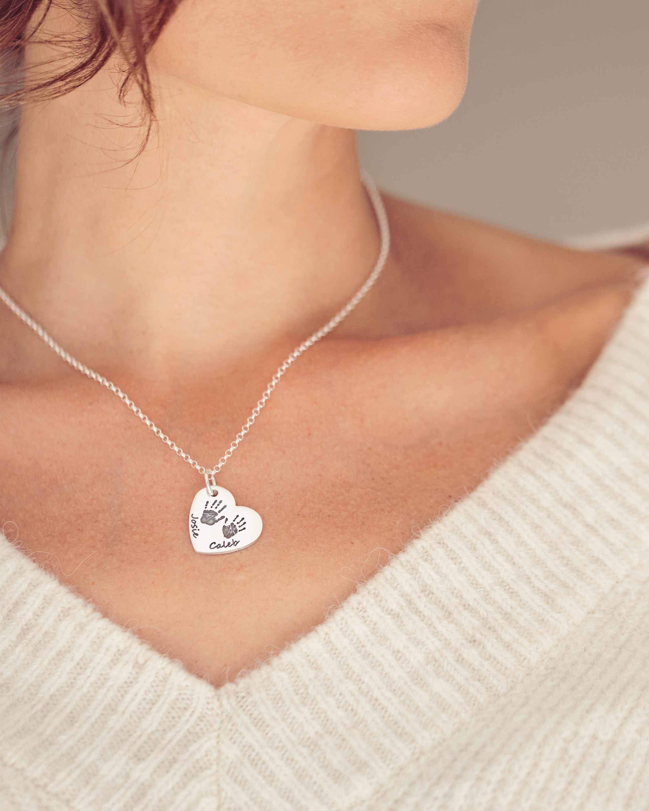A Silver heart necklace with two handprints on the front