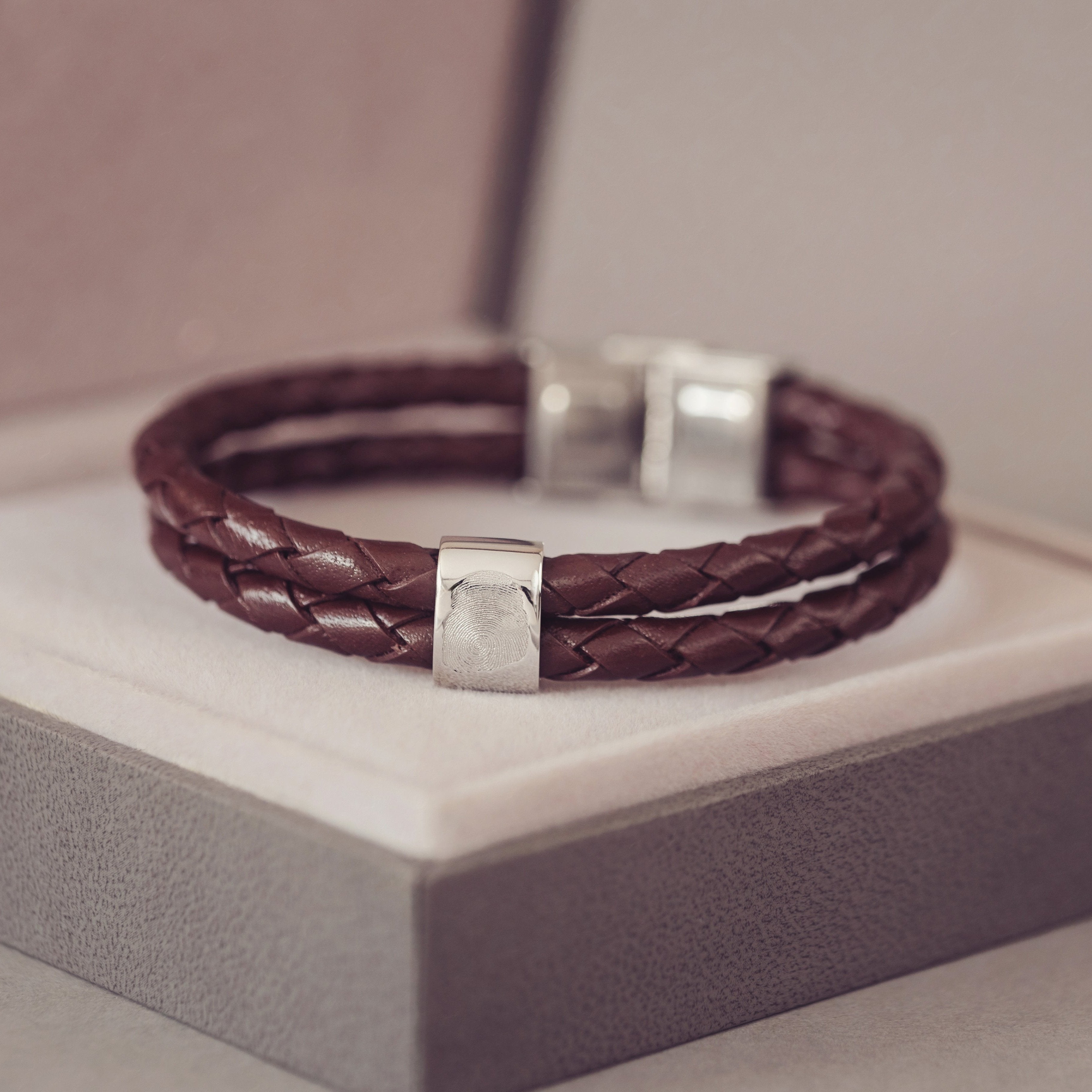 A brown leather bracelet with silver bar featuring fingerprint, resting on jewellery box