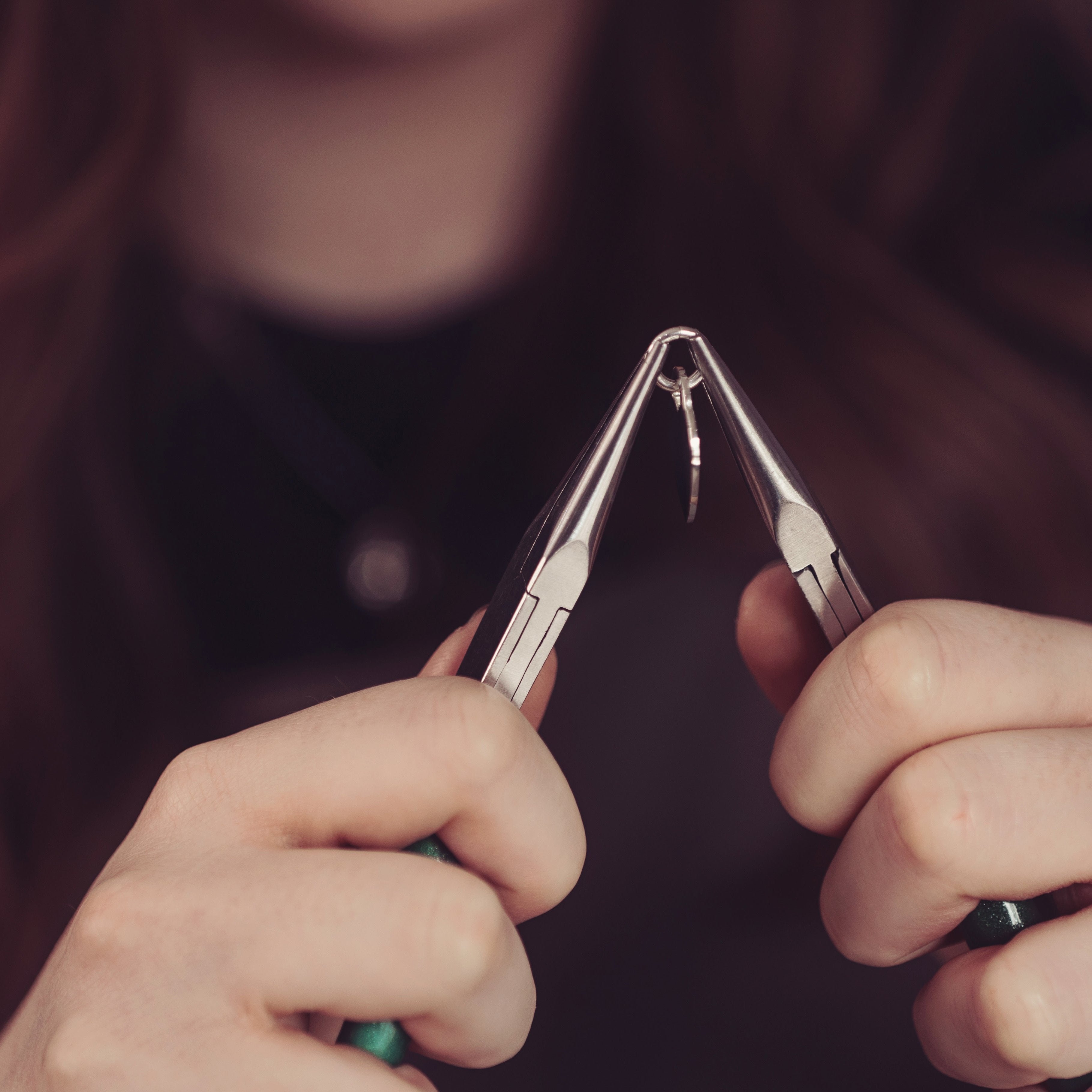 A team member holding a heart pendant with a pair of pliers