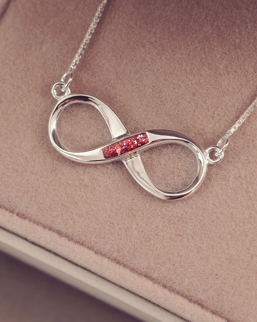 a sterling silver necklace pendant in an infinity symbol, the middle of which is filled with ref crystal and cremation ashes