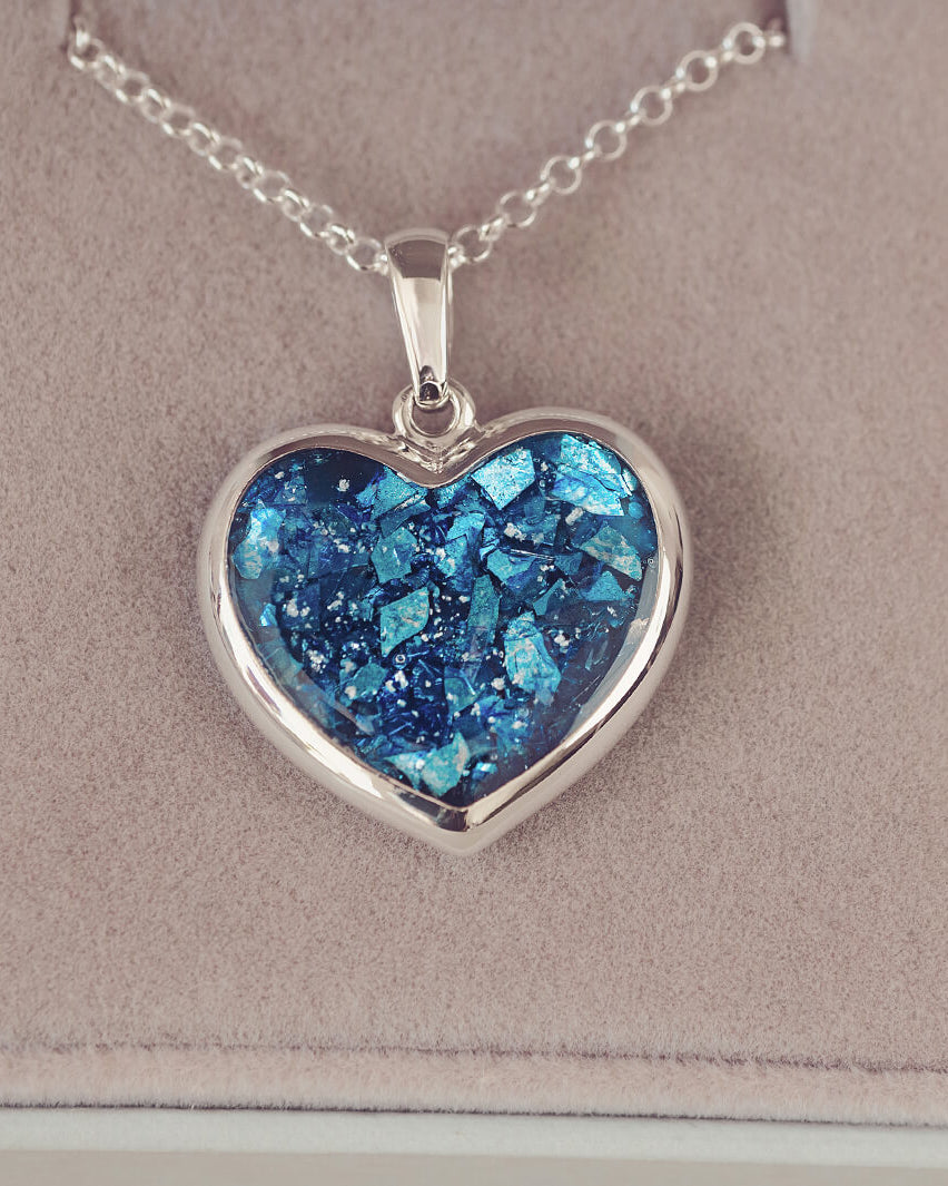 Sterling silver Large Heart necklace with a central section filled with memorial ashes and blue crushed crystals, displayed on a beige background.