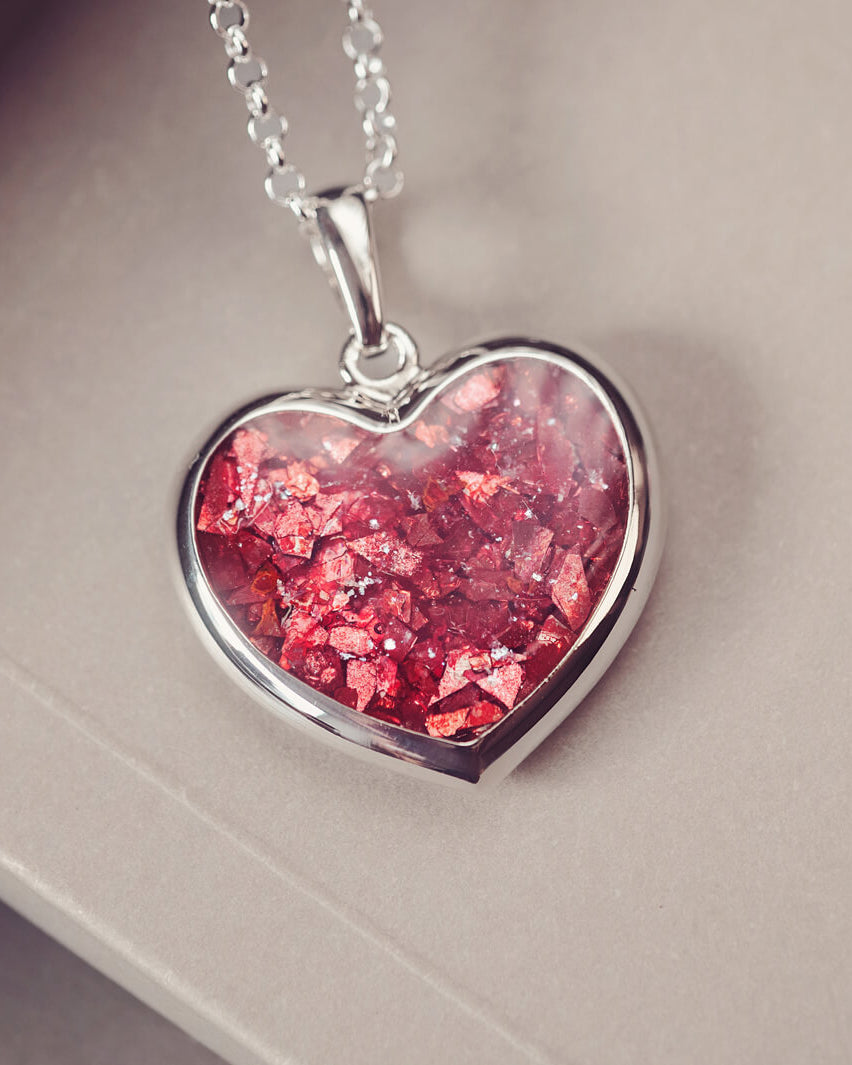 A sterling silver large heart pendant, hanging on a sterling silver belcher chain. The centre of the heart is filled with red crystal and ashes.
