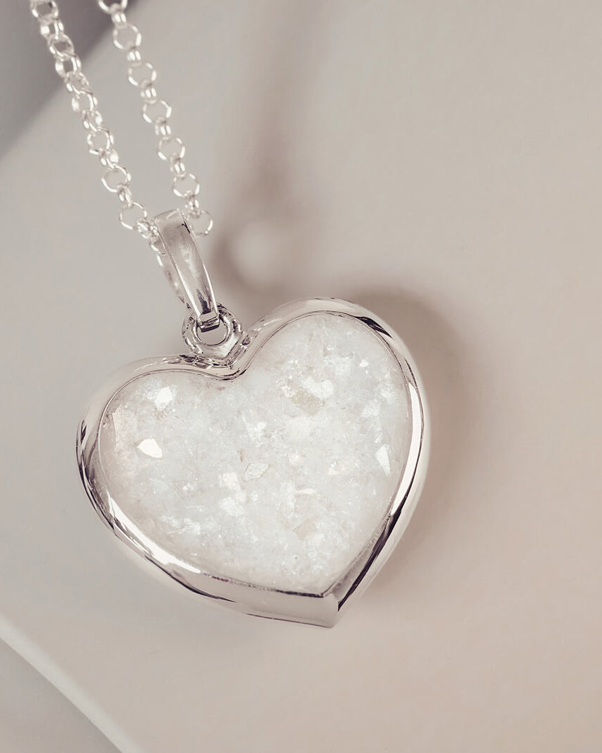 Sterling silver Large Heart necklace with a central section filled with memorial ashes and clear crushed crystals, displayed on a pale pink background.