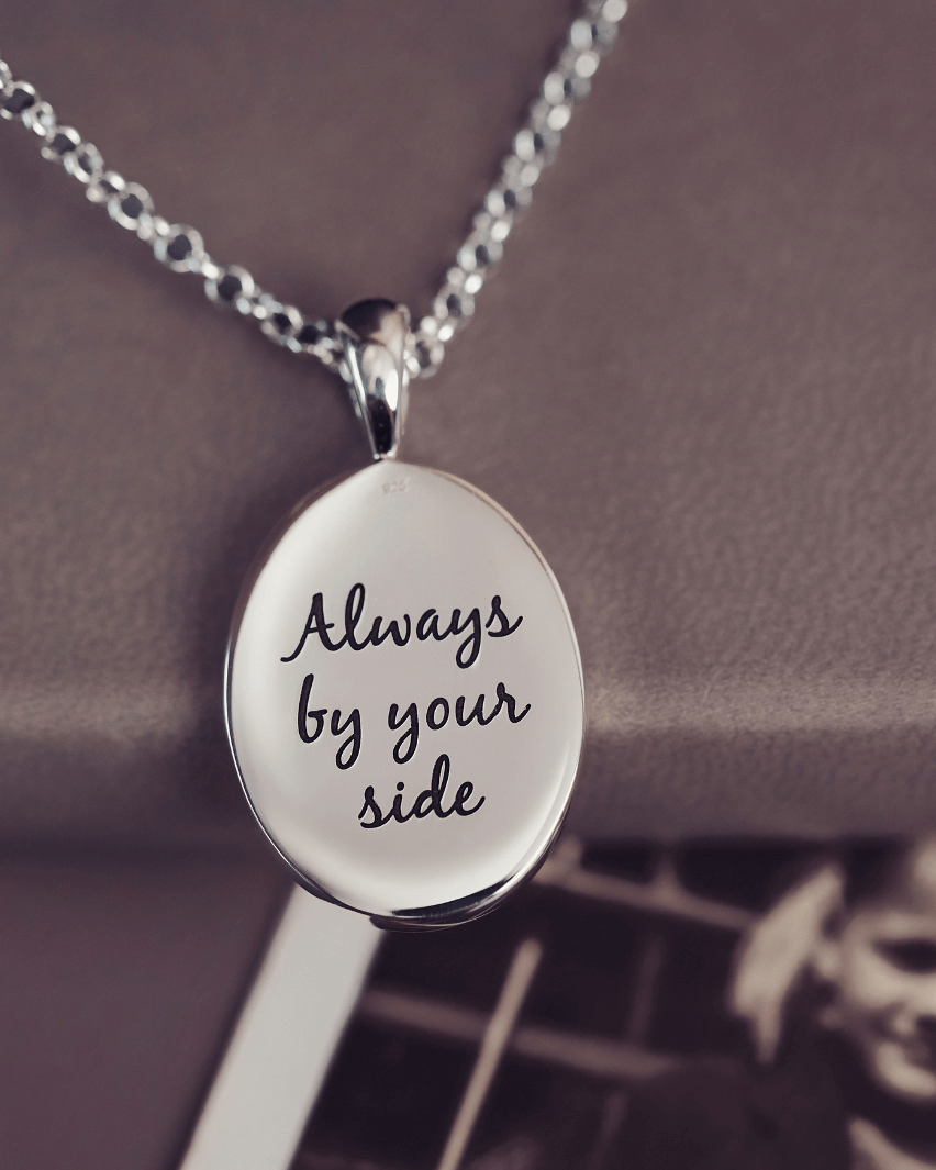 The reverse of a sterling silver Cremation Ashes Oval Necklace which has a message reading 'Always by your side' engraved into the pendant