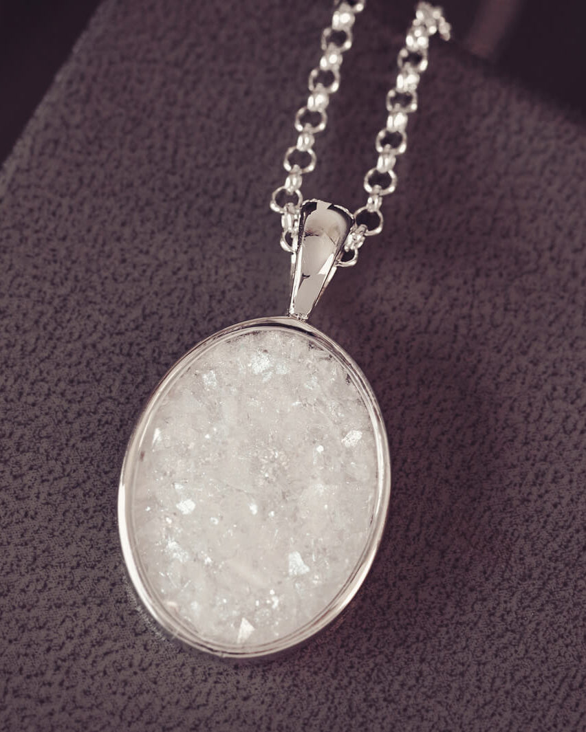 Sterling silver oval necklace with a central section filled with memorial ashes and white and clear crushed crystals, displayed in a grey jewellery box