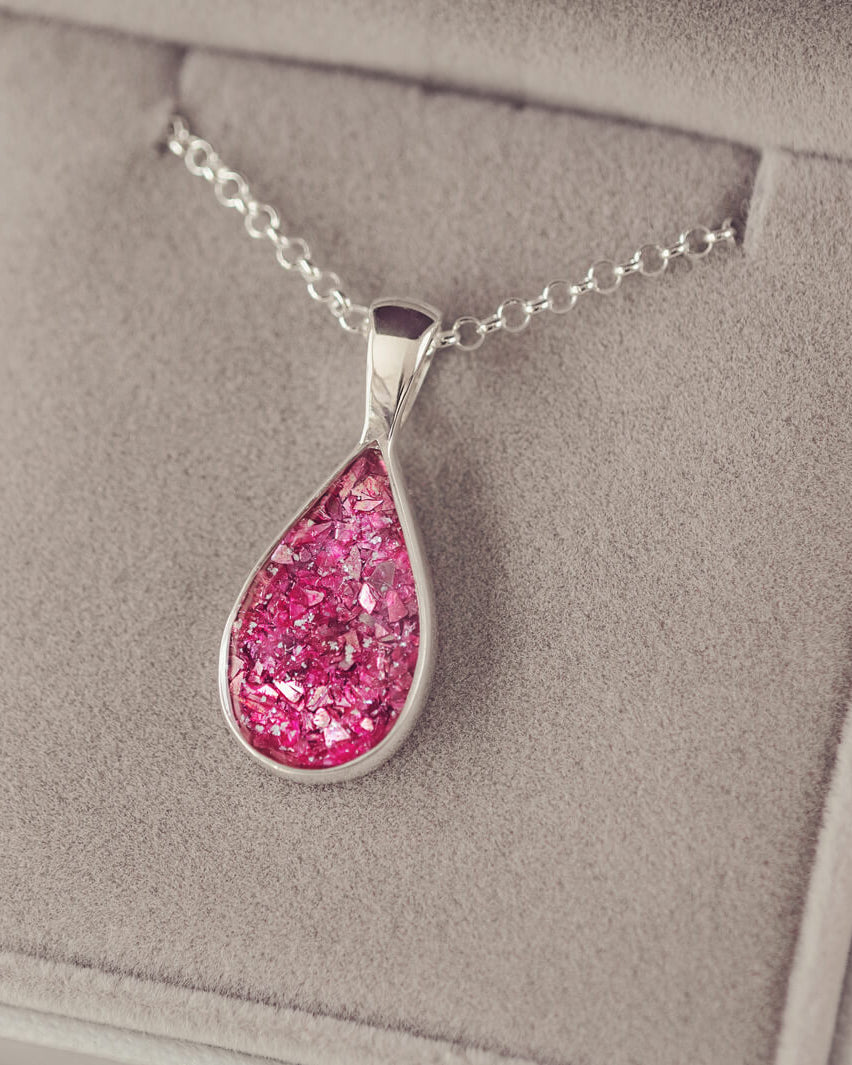 Sterling silver teardrop necklace with a central section filled with memorial ashes and pink crushed crystals, displayed in a grey jewellery box