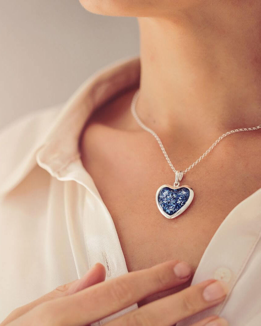 Close up of a lady wearing a Sterling silver Large Heart necklace with a central section filled with memorial ashes and blue crushed crystals.