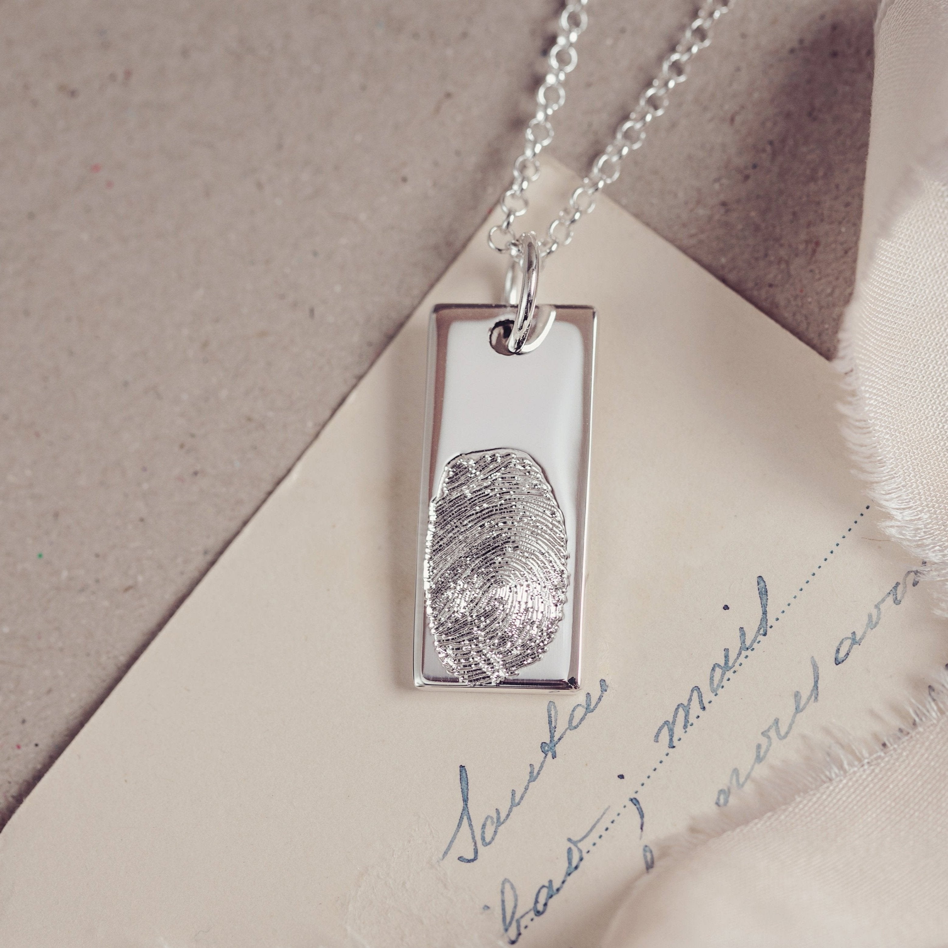 A close-up of a tag necklace intricately engraved with a detailed fingerprint, displayed on a handwritten letter