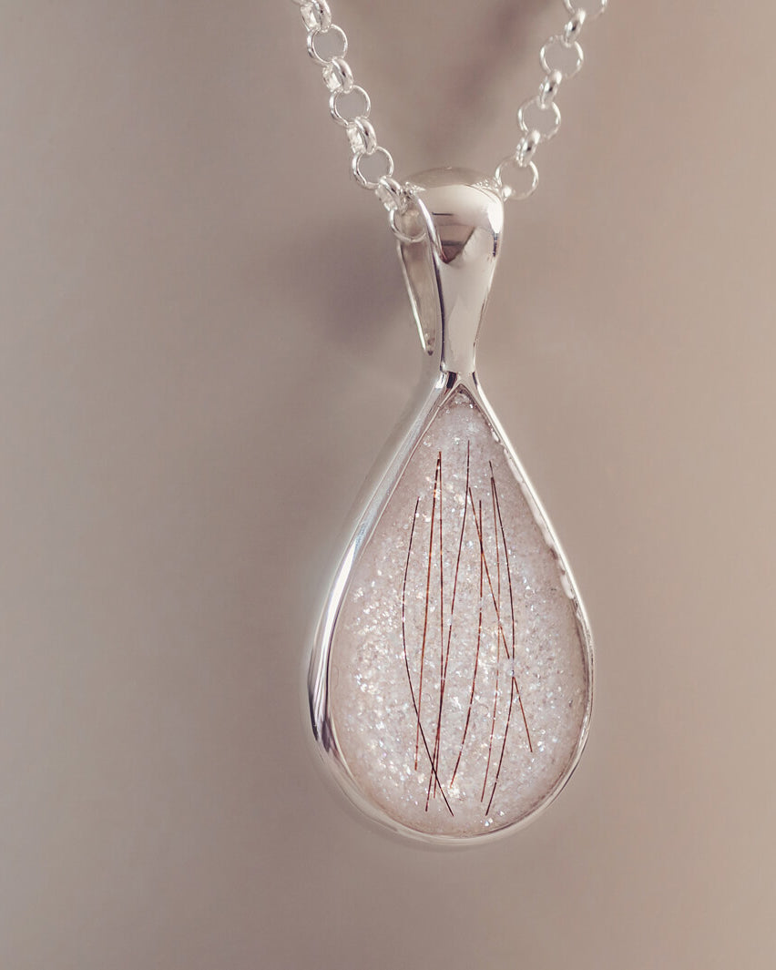 A silver teardrop necklace, filled with white glitter and strands of hair