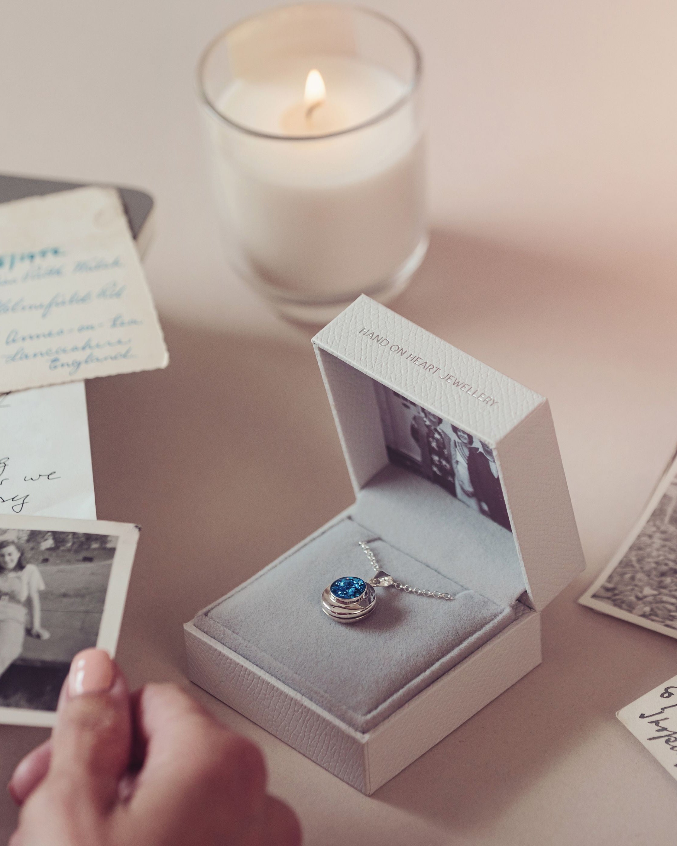 blue cremation ashes locket in a grey jewellery box and a womans hand holding a photograph