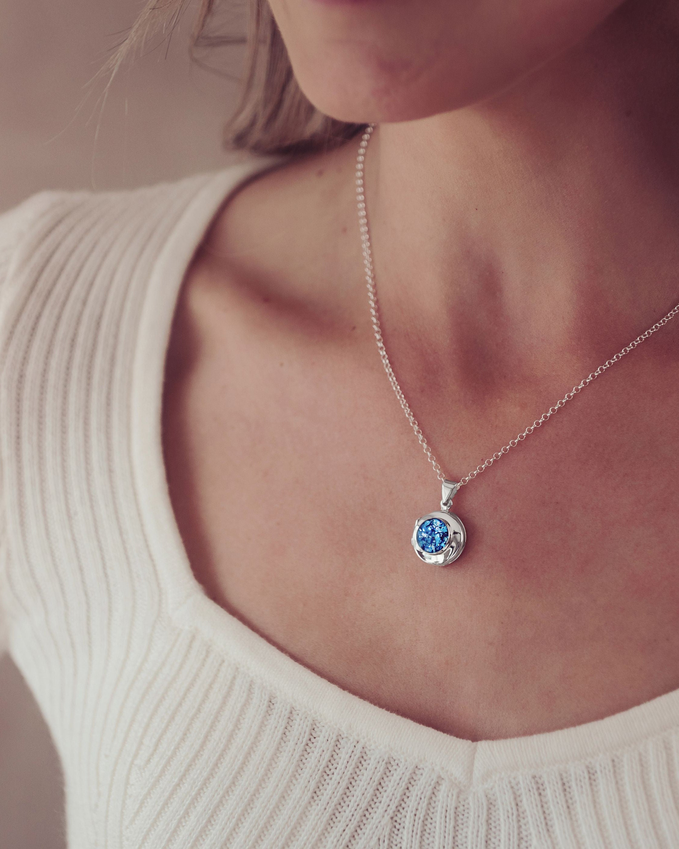 a silver and blue locket necklace filled with cremation ashes worn on a blonde lady's neck