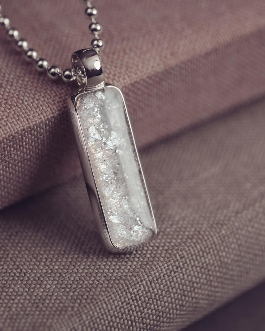 A sophisticated Mens silver necklace featuring a rectangular pendant filled with shimmering white crystal and resin, delicately layered with cremation ashes, showcased against a dark background on a silver ball chain