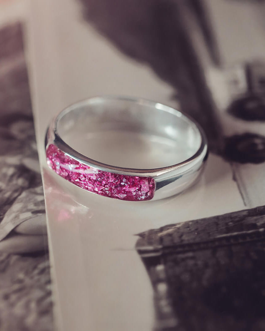 Sterling silver Mens Band Ring with a central section filled with memorial ashes and pink crushed crystals, displayed on top of an old photo