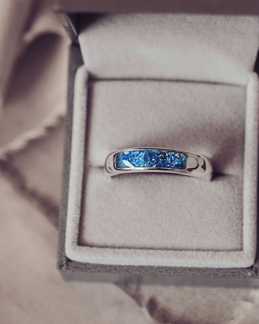 Sterling silver Mens Band Ring with a central section filled with memorial ashes and blue crushed crystals, displayed in a grey jewellery box
