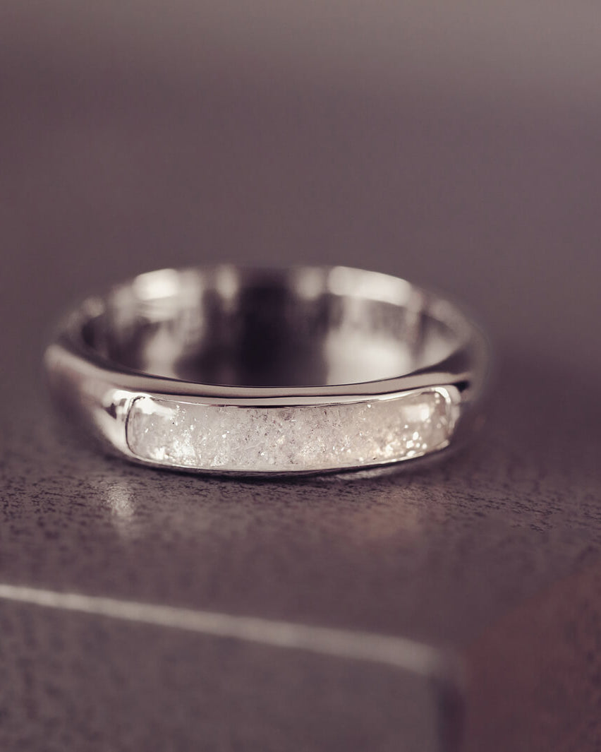Sterling silver Mens Band Ring with a central section filled with memorial ashes and clear crushed crystals, displayed on a grey jewellery box
