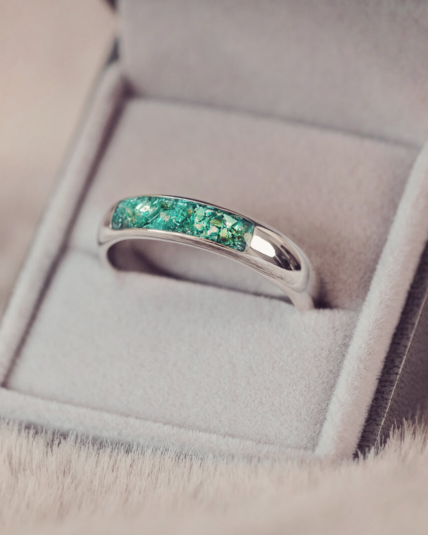 Sterling silver Mens Band Ring with a central section filled with memorial ashes and green crushed crystals, displayed in a grey jewellery box