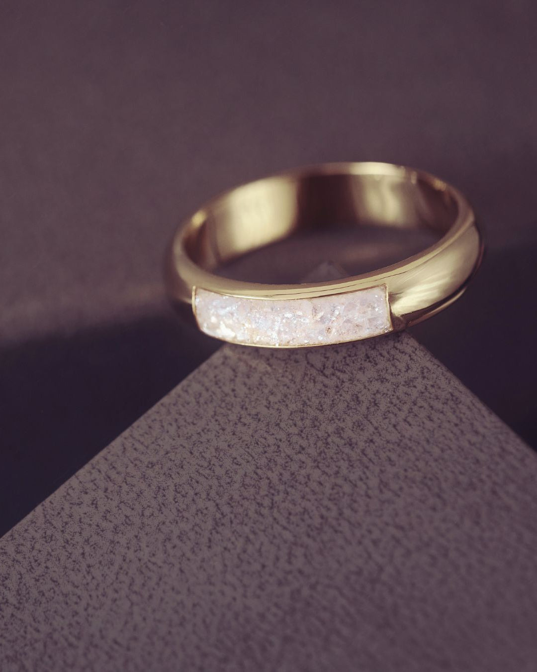 Gold ring with embedded stones on a textured purple surface