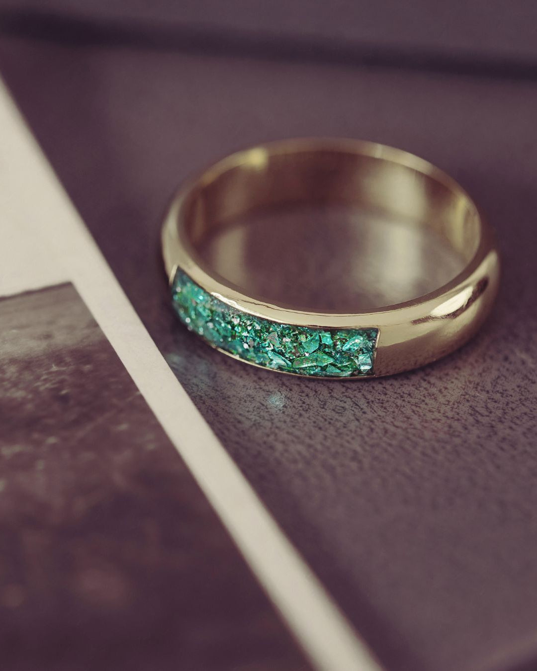 Gold ring with green gemstones on a textured surface