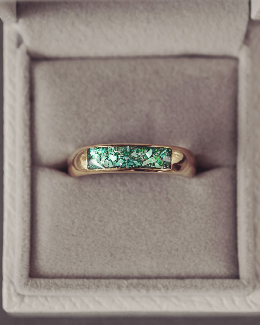 Gold ring with green gemstone in a gray jewelry box