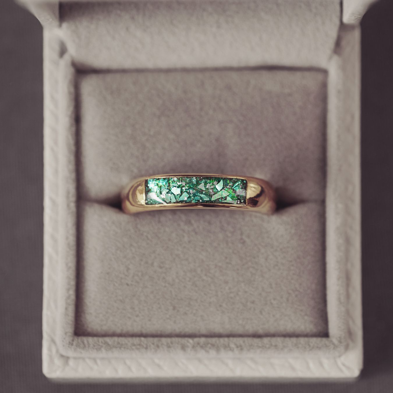 Gold ring with green gemstone in a gray jewelry box