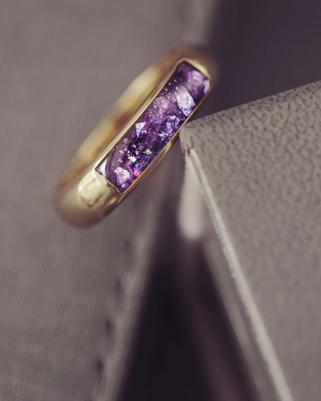 Gold ring with purple gemstone on a textured surface