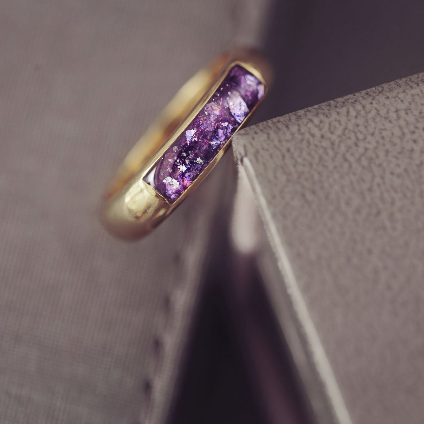 Gold ring with purple gemstone on a textured surface