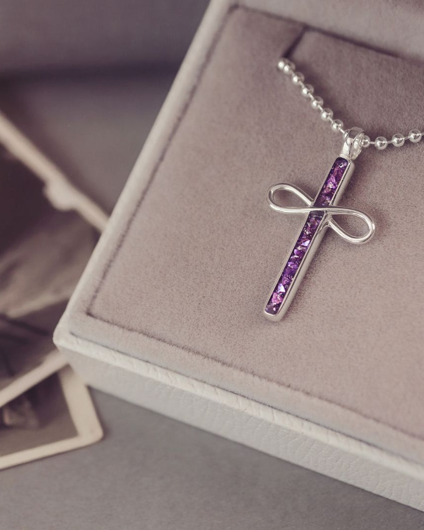 Silver cross necklace with purple stones on a display box