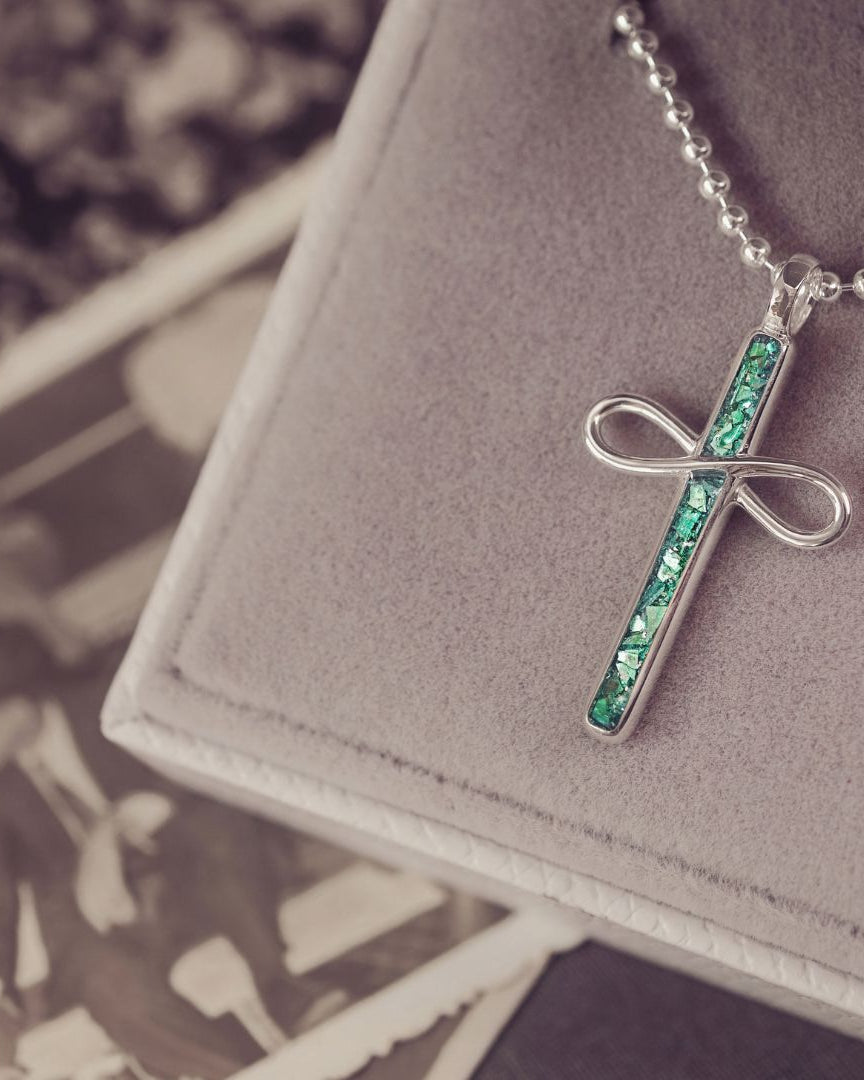 Necklace with a cross pendant featuring green stones on a gray surface.