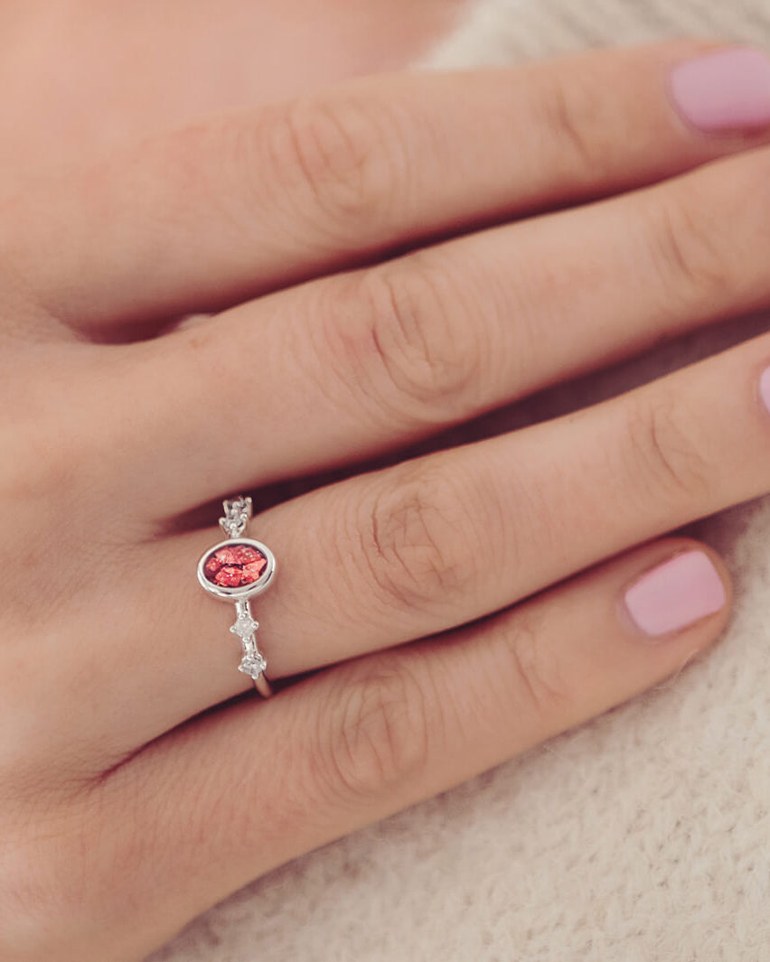 silver ring band with oval stone, created from cremation ashes & red crystal. Worn on a ladies hand.