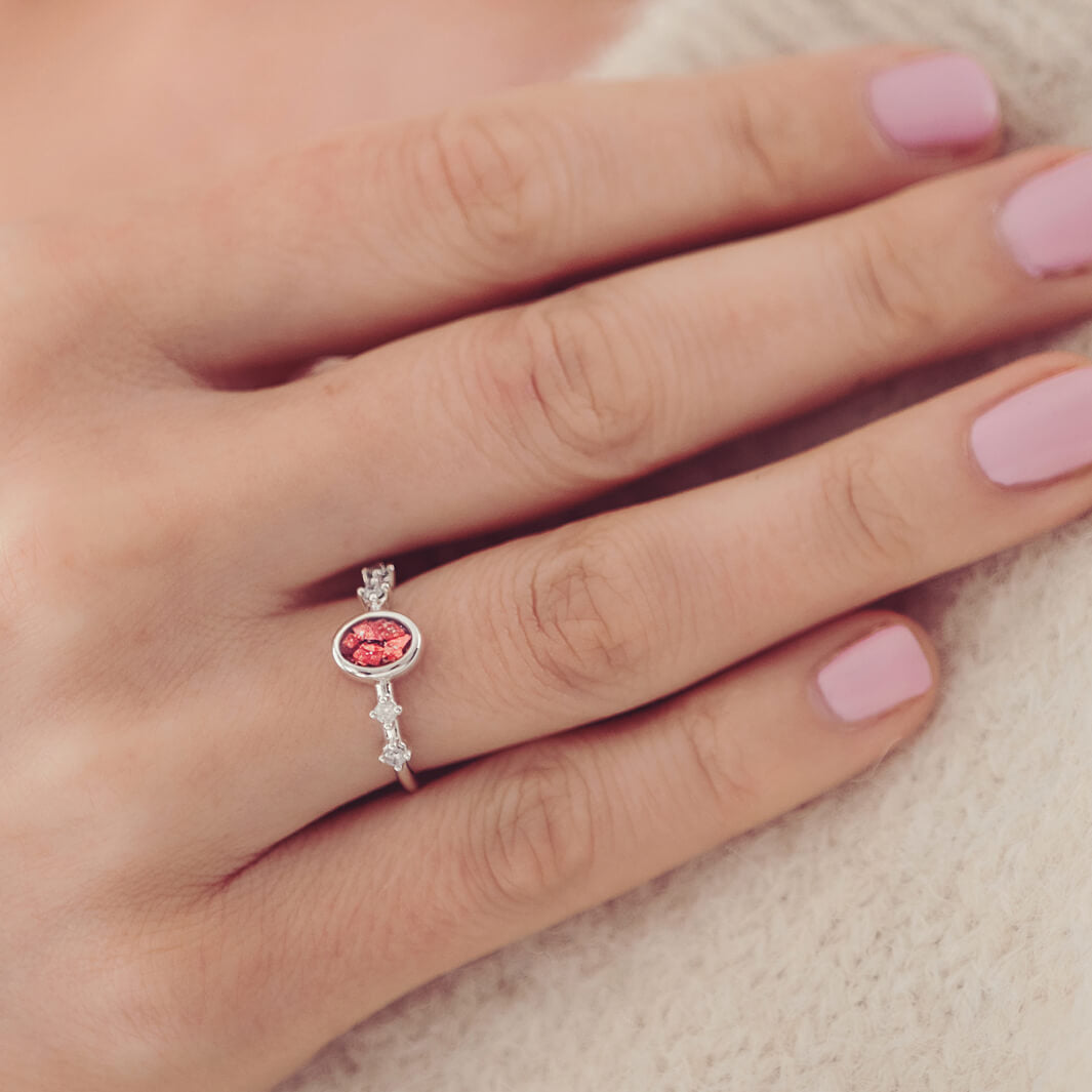 silver ring band with oval stone, created from cremation ashes & red crystal. Worn on a ladies hand.