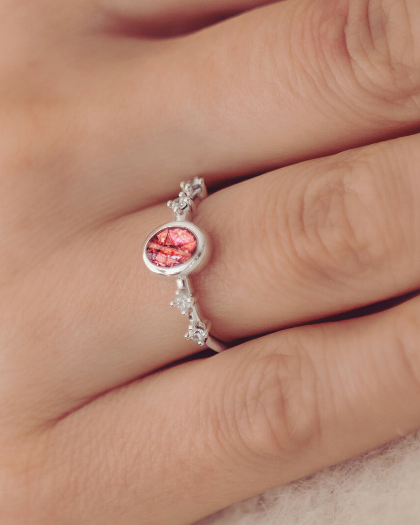 silver ring band with oval stone, created from cremation ashes & red crystal. Worn on a ladies hand.