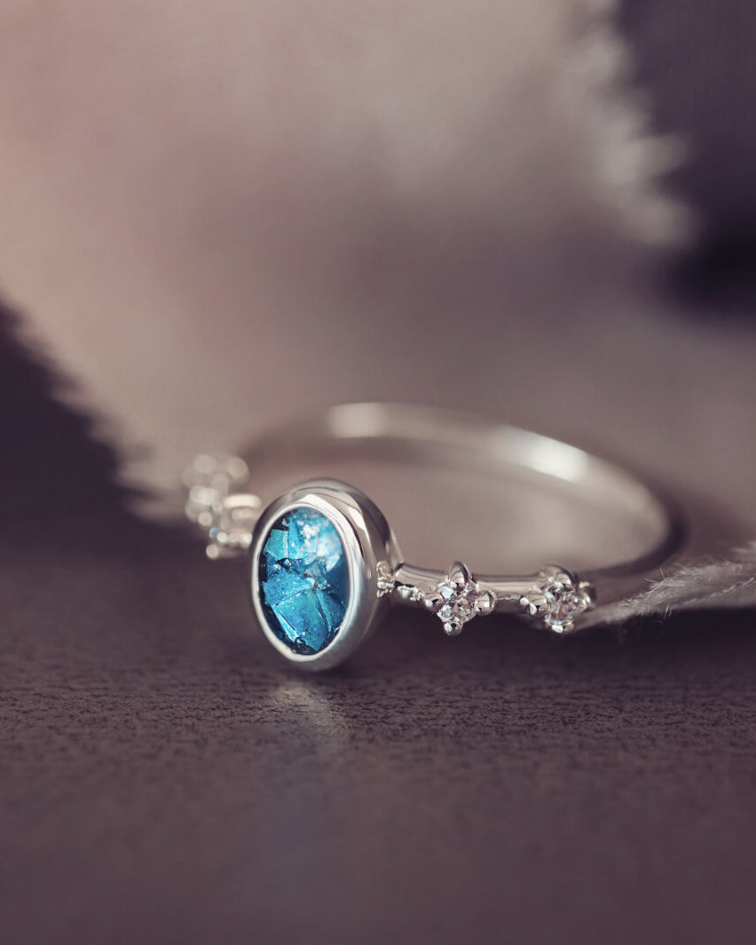 silver ring band with oval stone, created from cremation ashes & blue crystal. Sat on a dark grey background