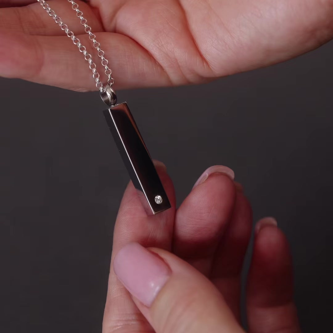 demo video of a silver bar ashes urn necklace. The video shows a women's hand unscrewing the necklace urn and filing it with ashes.