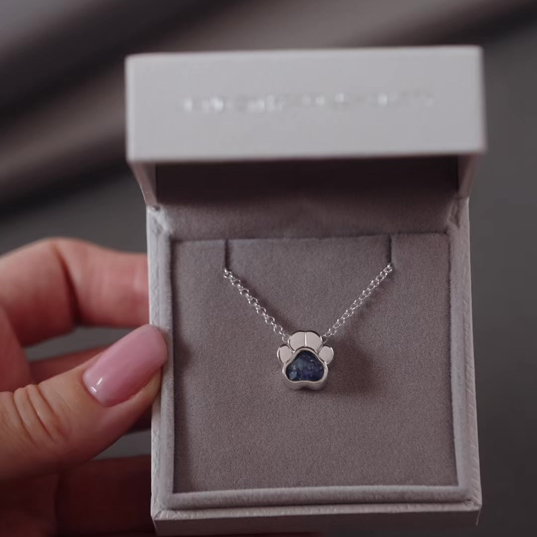 Silver ashes paw print necklace with blue crystals in a grey jewellery box held in a women's hand.
